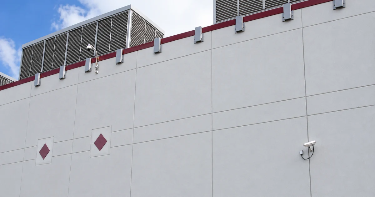 Exterior wall of a commercial building with rooftop ventilation equipment and security cameras under a blue sky.
