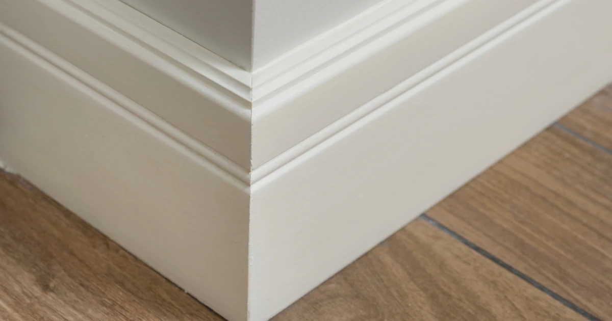 Close-up of a white painted baseboard and base molding meeting at an inside corner on a wood floor.