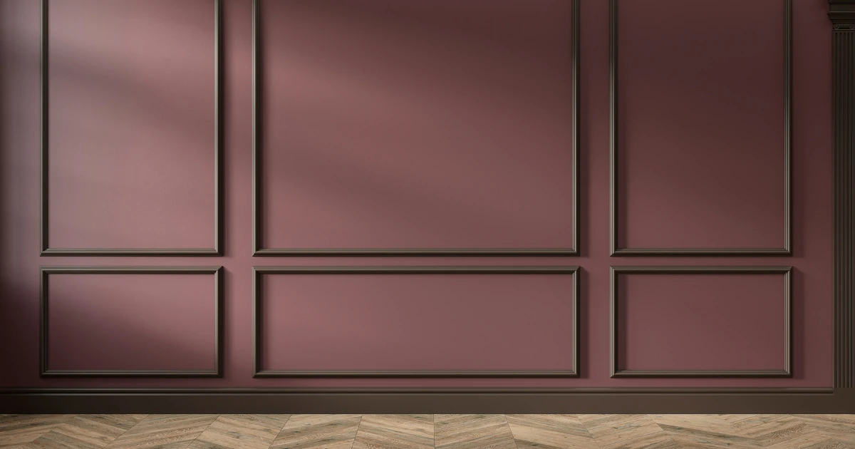 A wall painted deep mauve-brown with rectangular wainscoting panels framed in dark brown trim, above a herringbone wood floor.
