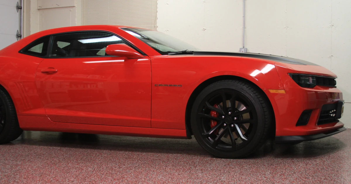 A red Chevrolet Camaro parked on a red-and-gray speckled garage floor coating.