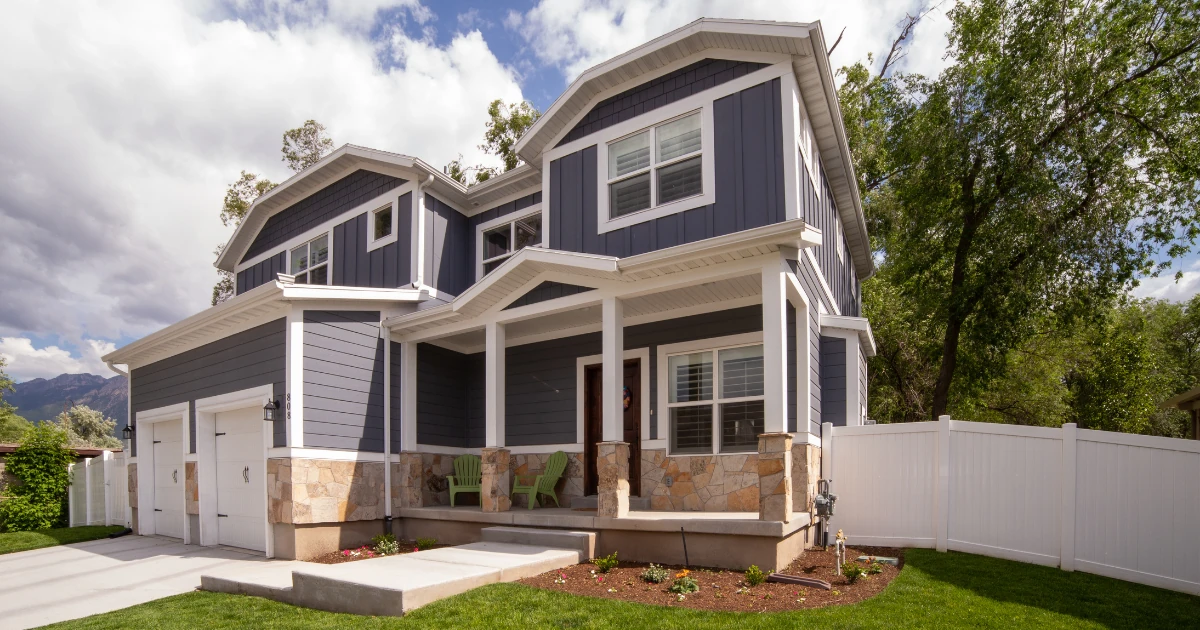 A completed two-story dark gray craftsman-style house with white trim, stone base accents, covered porch, attached garage, and landscaped front yard.