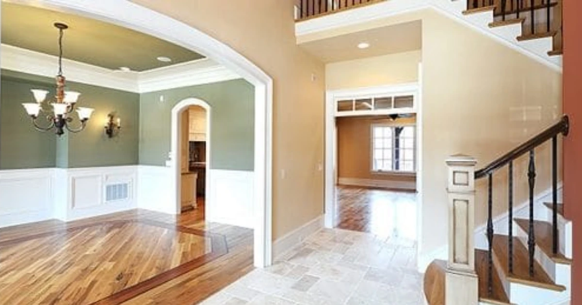 An open floor plan shows a sage-green dining room with a chandelier, a tan hallway, and a staircase with dark wrought-iron balusters.