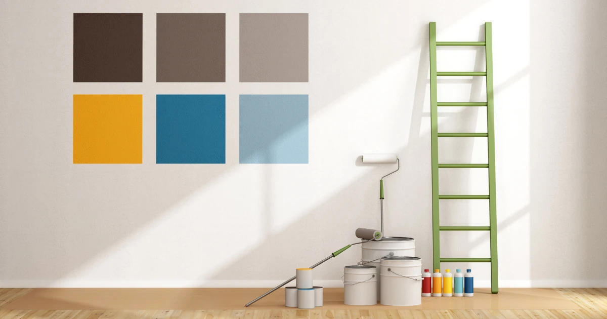 Six large paint swatches in browns, gold, and blues painted on a white wall beside paint cans, a roller, and a ladder.