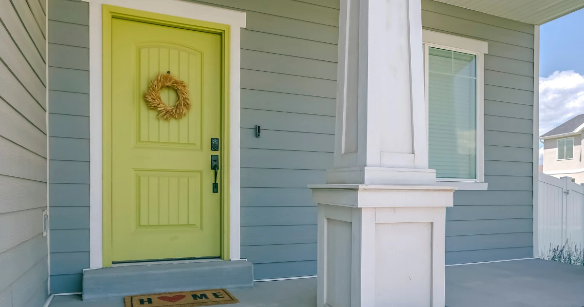 Front entry of a home with gray siding, white trim, and a bright yellow green painted door with a wreath.