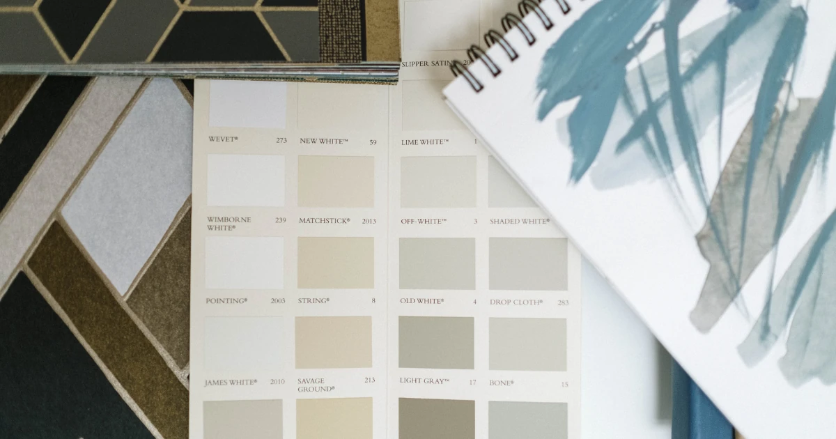 Neutral paint color cards in whites, creams, and soft grays laid out beside tile samples and a painted color study.