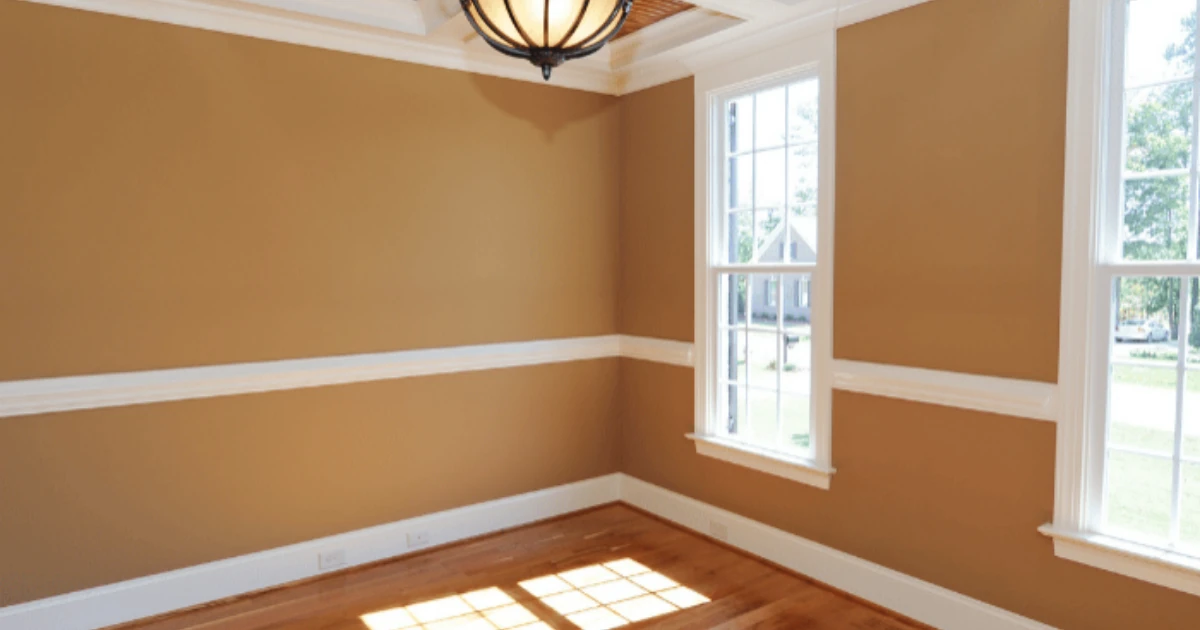 An empty room with warm tan walls, white chair rail and baseboard, white window casings, and a coffered ceiling with white beams.