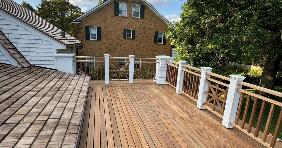 A restored wood deck with freshly finished decking, white painted posts, and natural wood railings overlooking a shingled roof and yard.