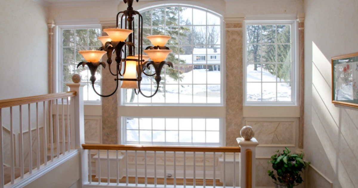 An interior stair landing with tall white framed windows looking out onto a snow covered yard.