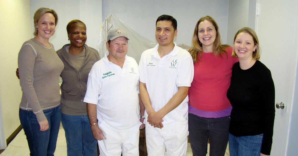An A.G. Williams Painting Company senior foreman and crew leader standing with four volunteers in the reception area during the community painting partnership.