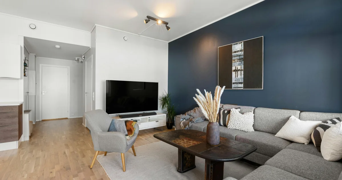 Living room with a dark blue painted accent wall behind a gray sectional sofa.