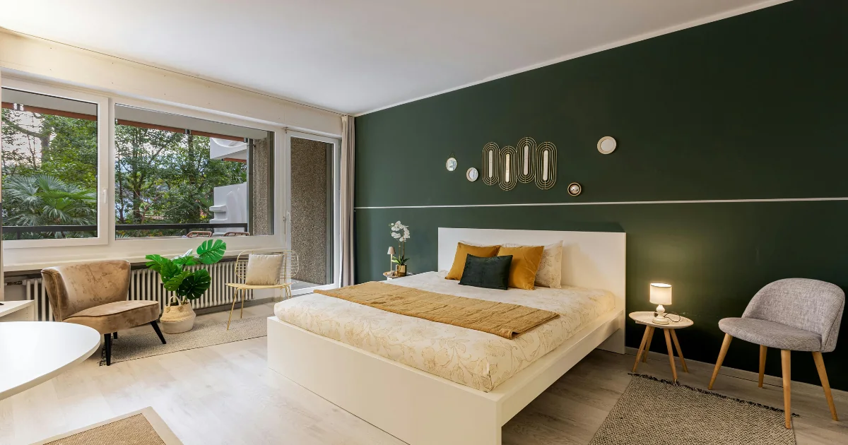 Bedroom with a dark green painted accent wall behind a white bed.