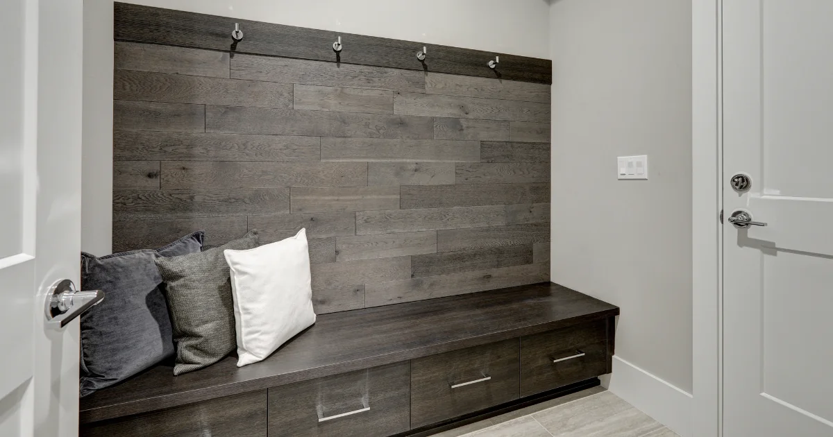 Mudroom bench backed by dark wood wall paneling and coat hooks.