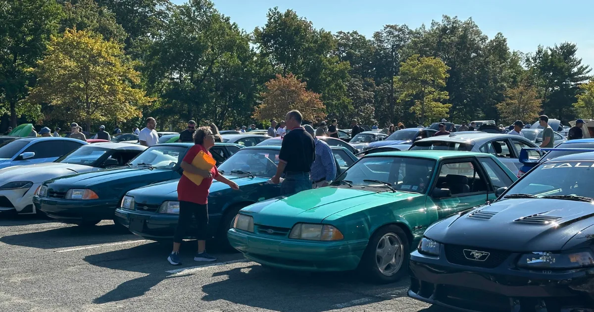 Rows of teal and black Ford Mustangs with attendees at the Rye Brook Cars & Coffee meetup.