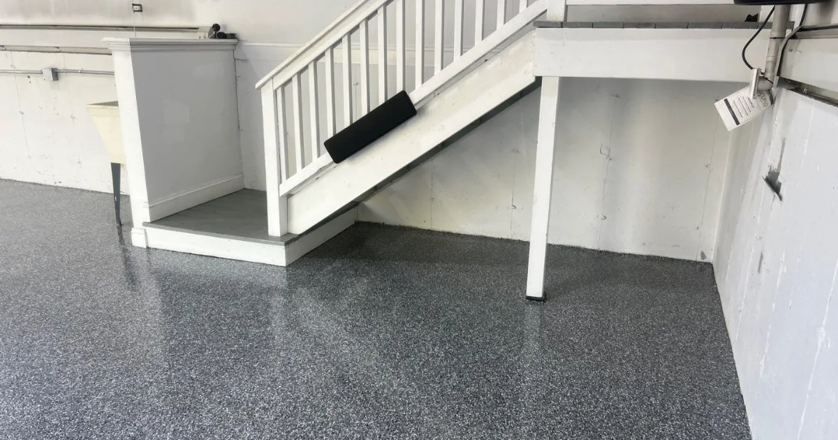 Finished gray flake basement floor coating around white stairs and support posts.