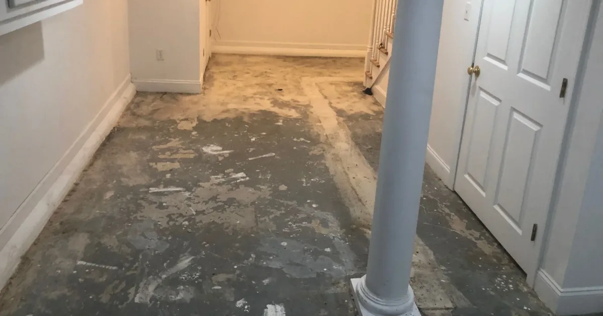 Basement concrete floor with old surface material exposed before mechanical preparation.