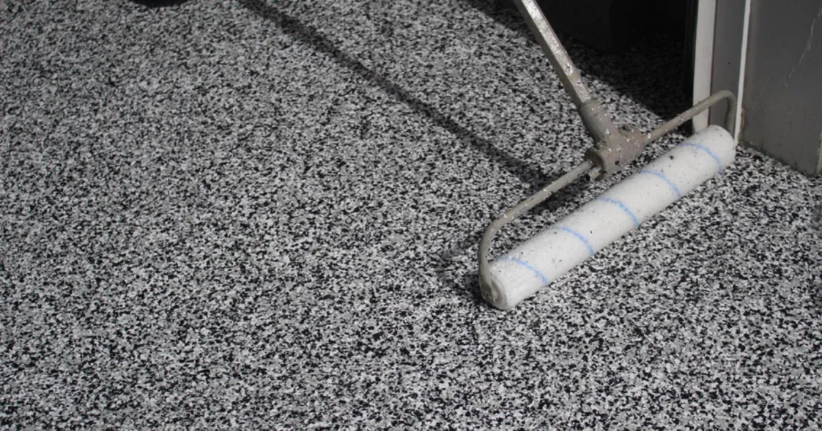 Roller applying a clear finish over a black-and-white flake floor coating.
