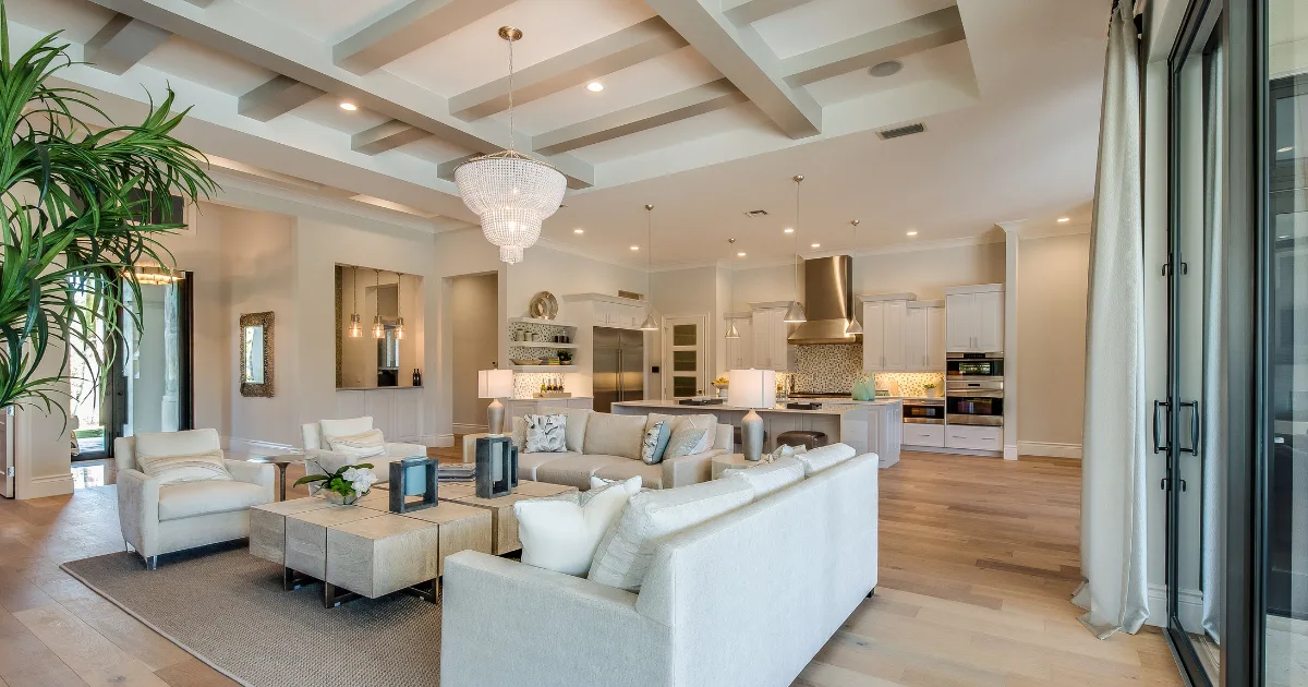 Warm neutral living room and kitchen connected beneath a coffered ceiling.