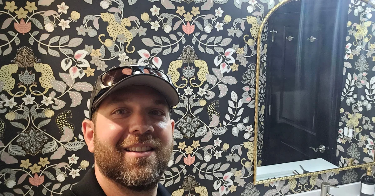 A.G. Williams team member standing in a powder room with high-contrast floral and leopard wallpaper.