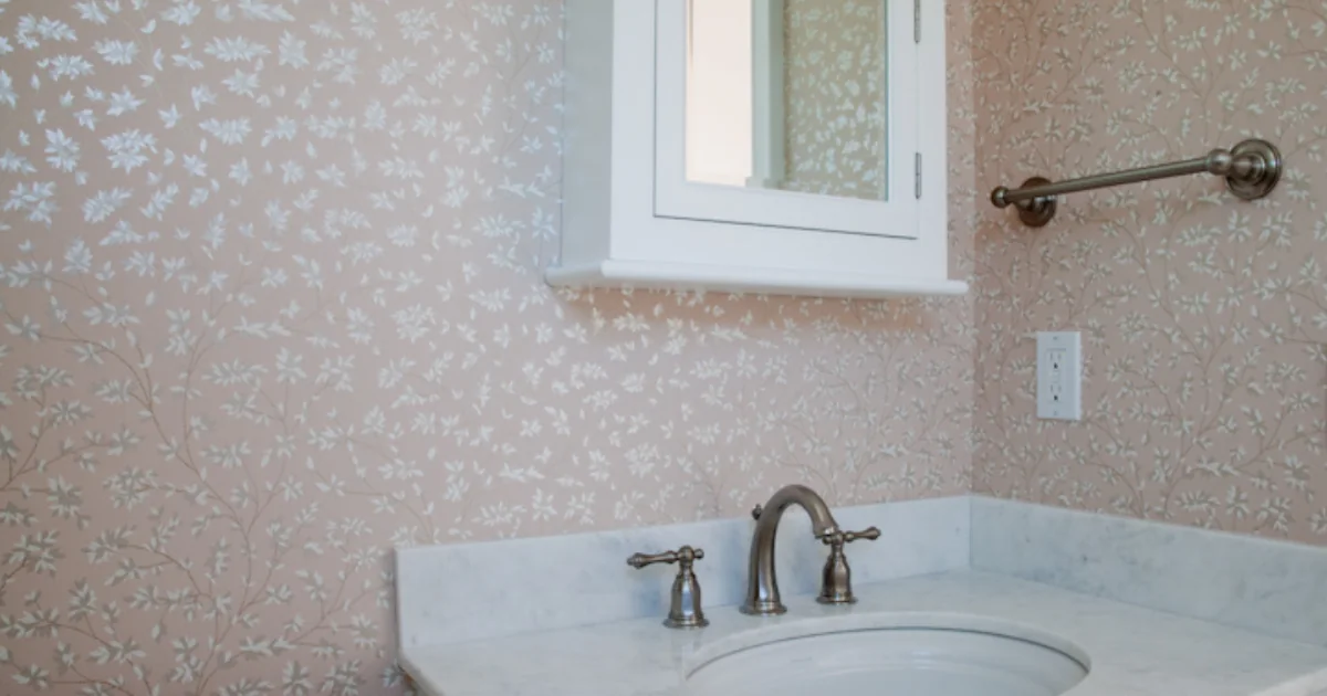 Powder room vanity beneath blush wallpaper with a white leaf pattern.