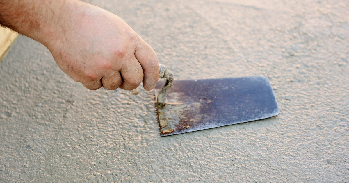 Worker smoothing fresh stucco with a metal finishing trowel.