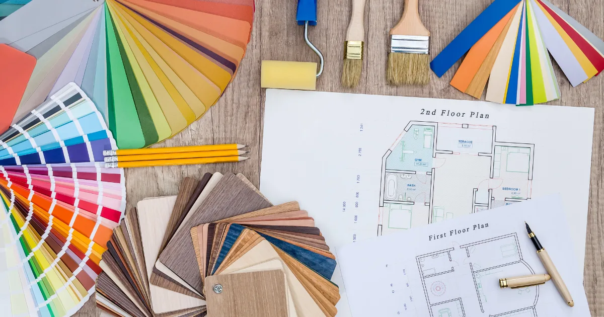 Floor plans, paint color swatches, wood samples, rollers, and brushes arranged on a table.