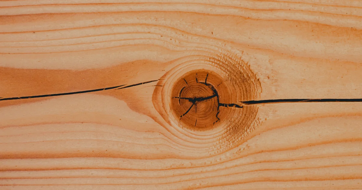 Close-up of a natural wood board with a dark, cracked knot in its grain.