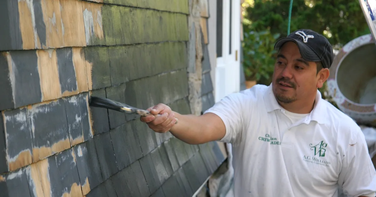 A.G. Williams painter applying a dark finish to cedar shingles with a brush.