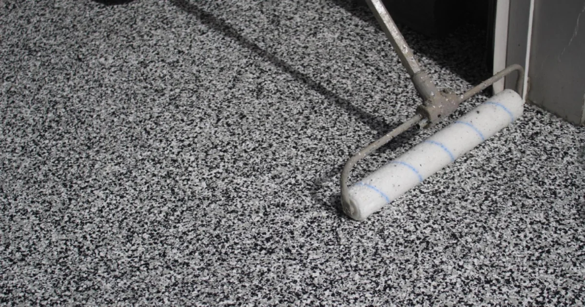 A roller applies a gray-and-black flake coating to a concrete floor at a doorway.