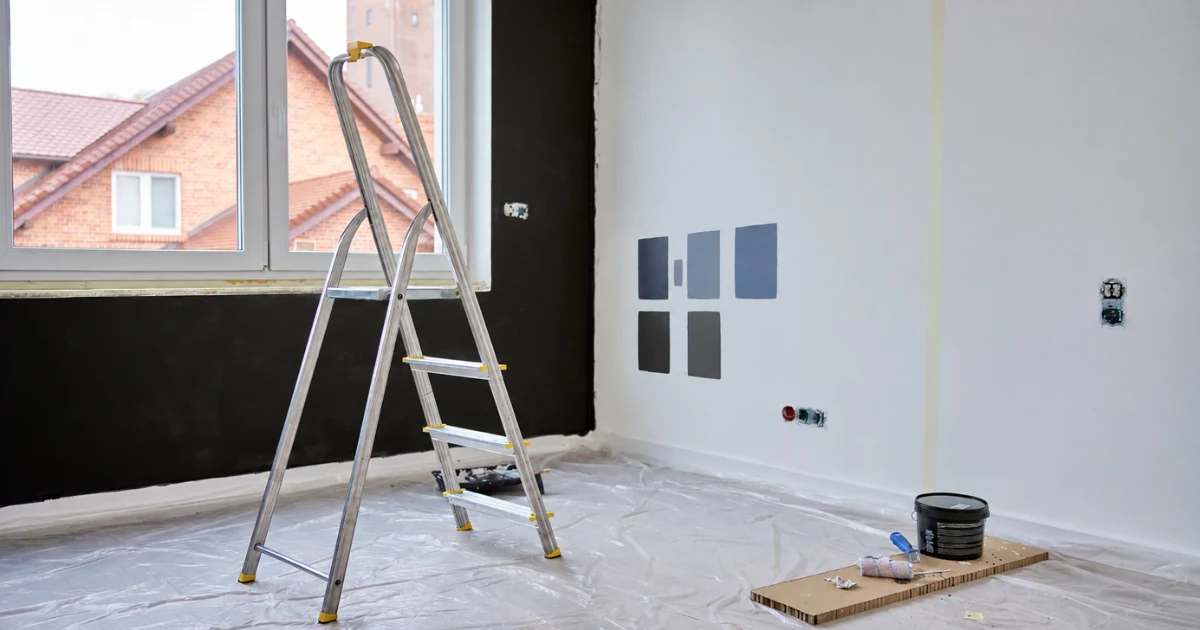 Interior room prepared for painting with a ladder and paint color samples on the wall.