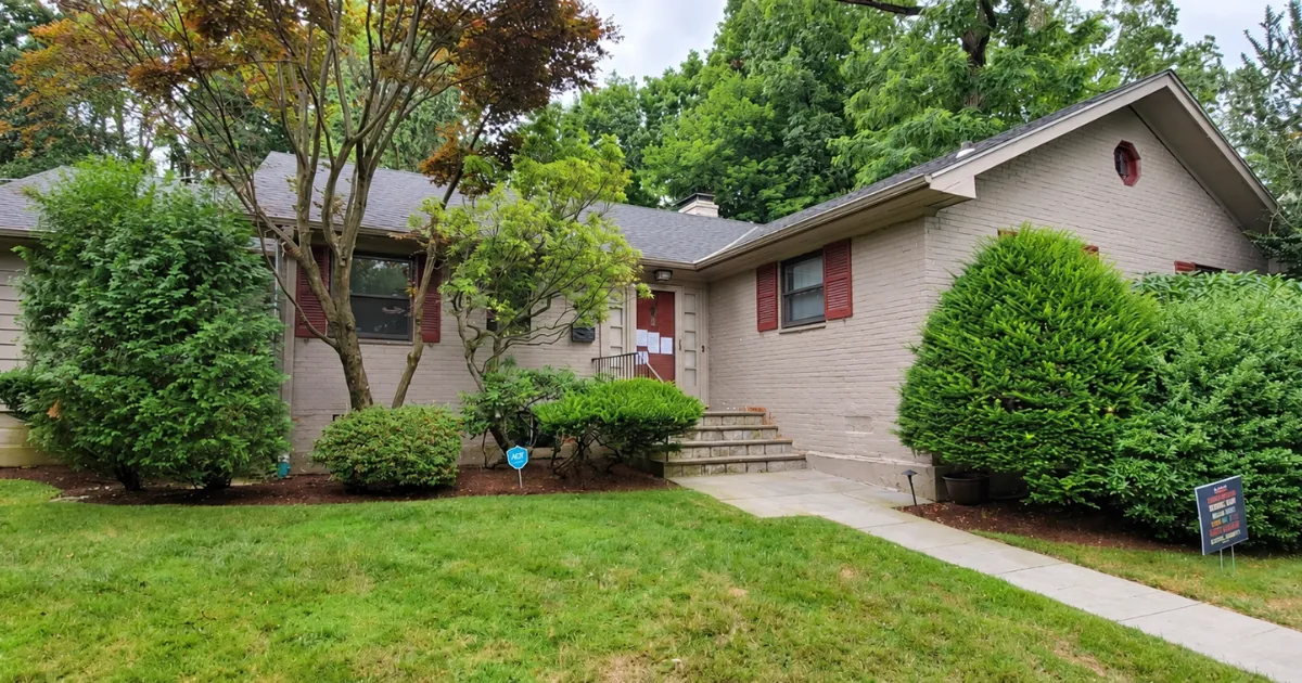 Painted brick ranch in faded gray with red shutters before exterior painting.