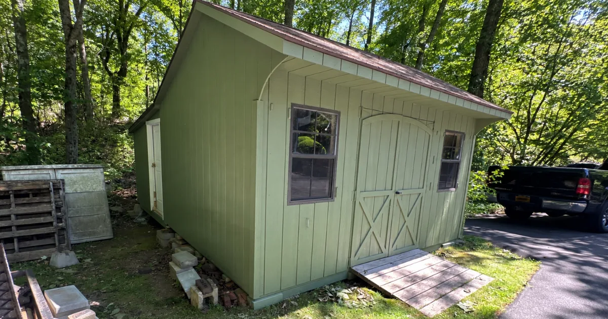 The same outbuilding after exterior painting in soft green with clean trim.