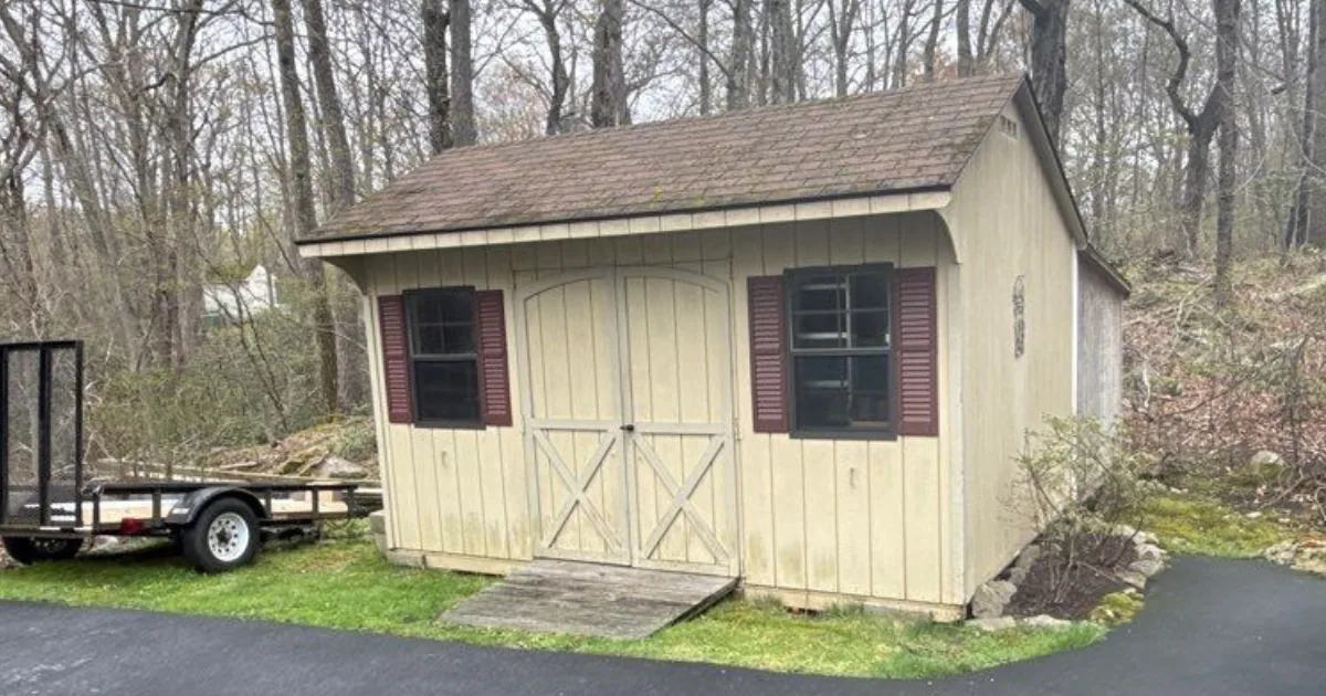 Outbuilding with faded, weathered siding and dark shutters before exterior painting.