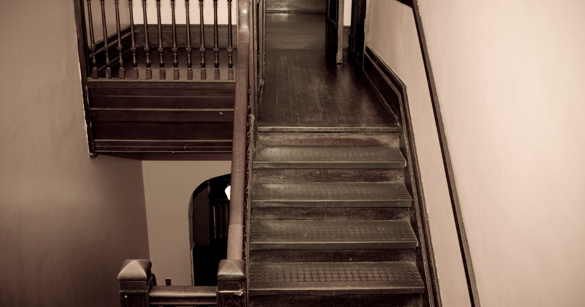 An older interior stairwell with dark wood railings, trim, and treads.