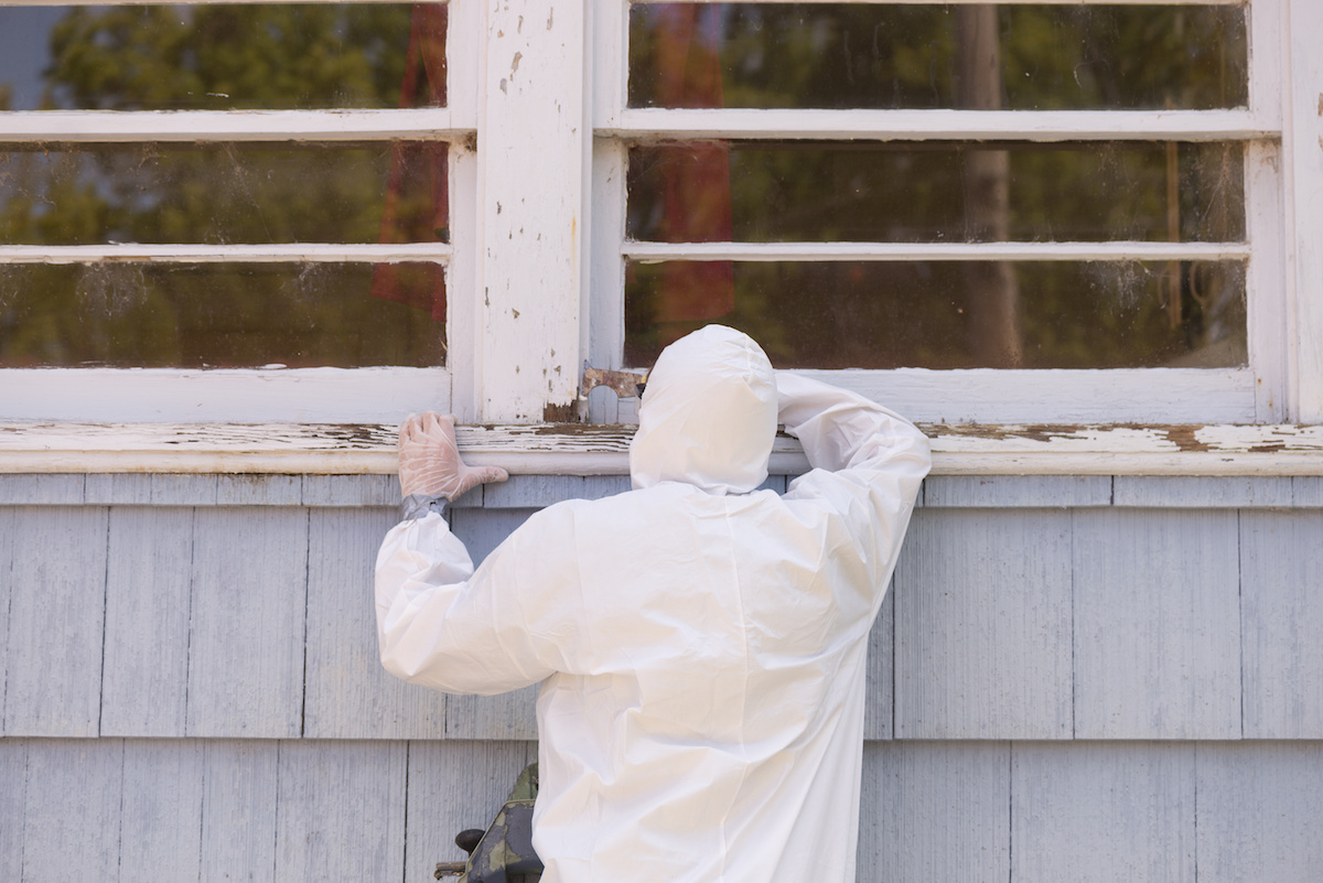 A protected worker inspecting deteriorated paint on an older window sill.