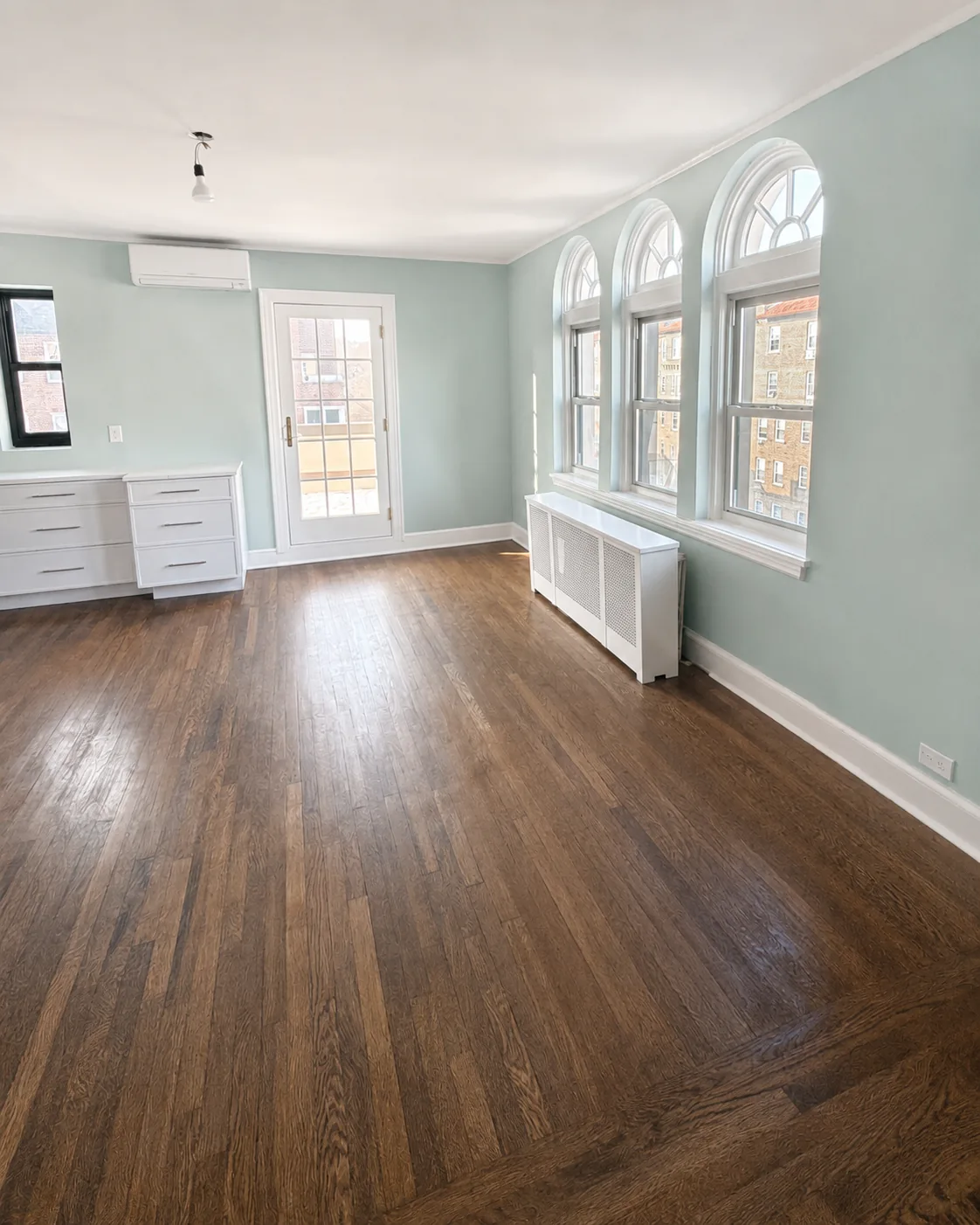 Light blue painted room with arched windows, white trim, and wood floors in Larchmont.